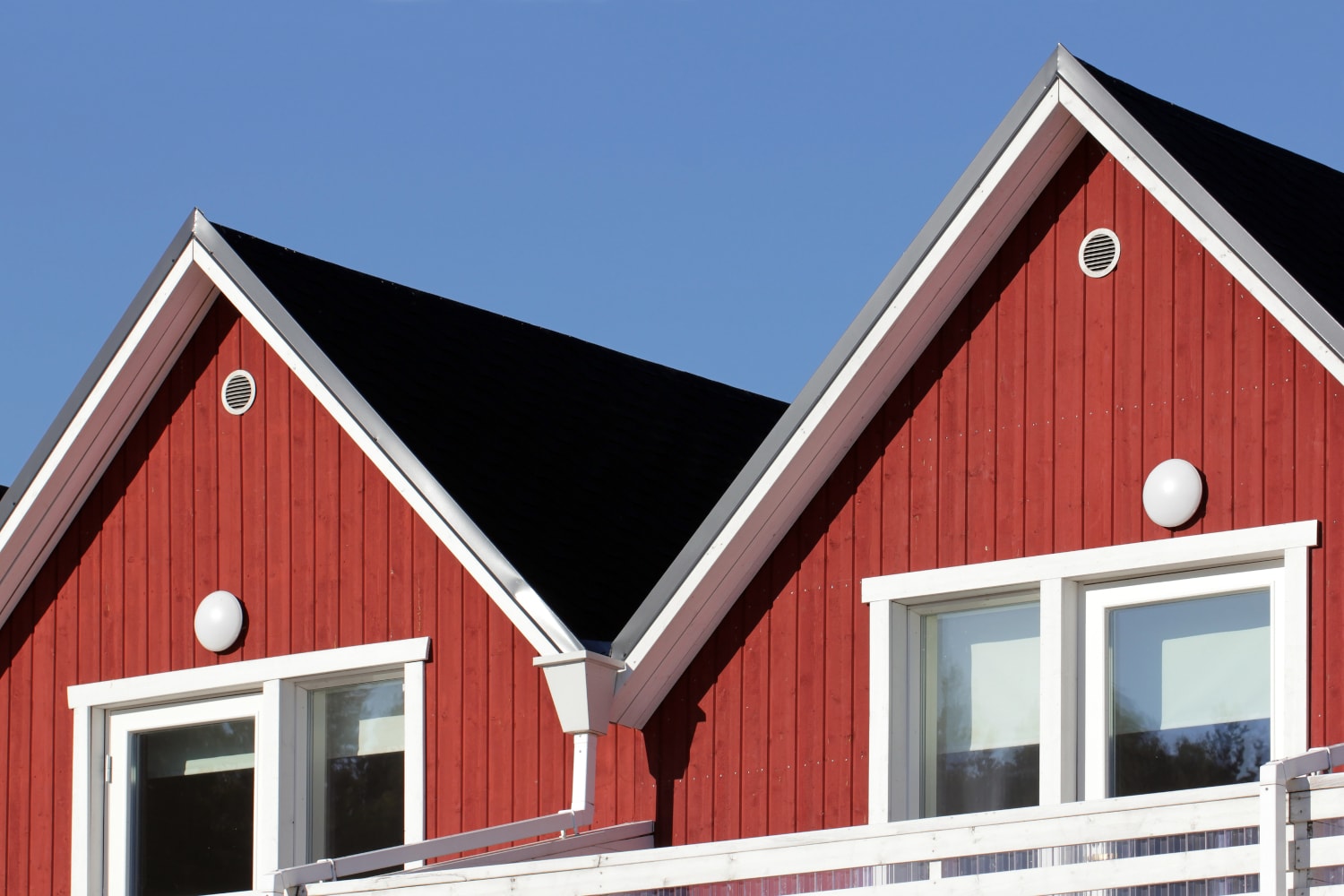 Röda parhus med vita knutar och svart plåttak mot blå himmel en solig dag